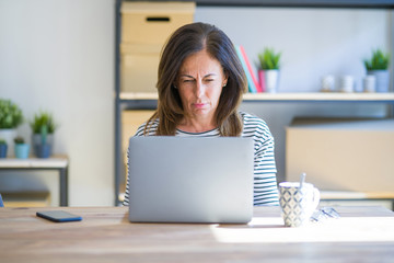 Middle age senior woman sitting at the table at home working using computer laptop skeptic and nervous, frowning upset because of problem. Negative person.