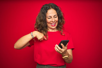 Naklejka premium Middle age senior woman using smartphone over red isolated background with surprise face pointing finger to himself