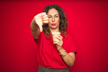 Middle age senior woman drinking a cup of coffee over red isolated background with angry face, negative sign showing dislike with thumbs down, rejection concept