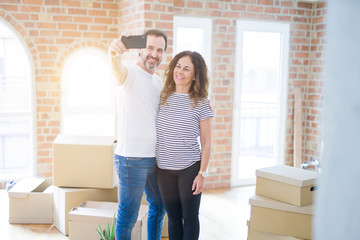 Fototapeta na wymiar Middle age senior romantic couple taking a selfie picture with smartphone smiling happy for moving to a new house, making apartment memories