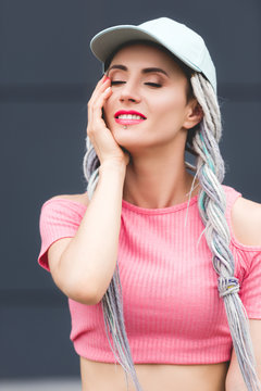 beautiful stylish smiling girl with dreadlocks in hat touching face