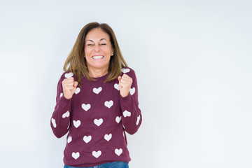 Beautiful middle age woman wearing heart sweater over isolated background excited for success with arms raised celebrating victory smiling. Winner concept.