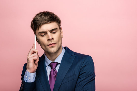 thoughtful businessman in formal wear talking on smartphone isolated on pink
