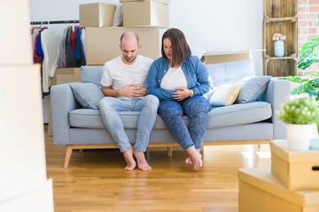 Fototapeta na wymiar Young couple sitting on the sofa arround cardboard boxes moving to a new house with hand on stomach because indigestion, painful illness feeling unwell. Ache concept.