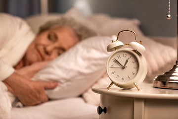 Alarm clock on table of sleeping senior woman at night - Powered by Adobe