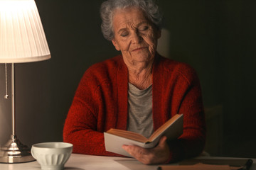 Senior woman reading book at night