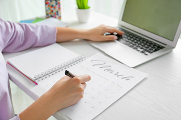 Young woman marking date in calendar at table, closeup