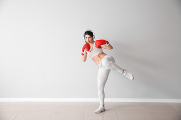 Sporty female kickboxer with headphones near white wall