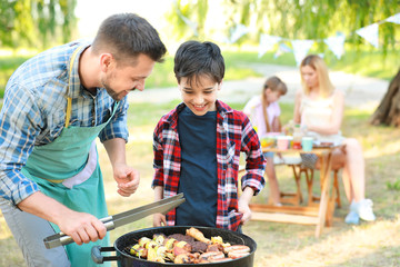 Little boy with father cooking tasty food on barbecue grill outdoors
