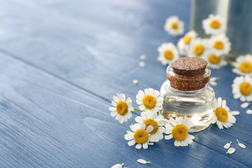 Bottle of essential oil with chamomile flowers on wooden table