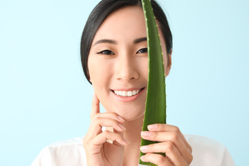 Beautiful Asian woman with aloe vera on color background
