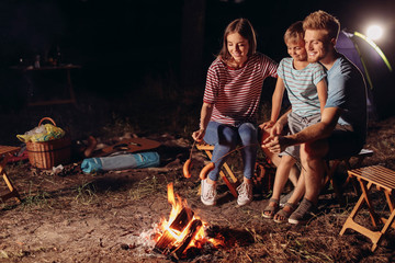 Family roasting sausages over campfire in evening