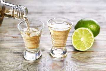 Pouring of tequila in glass on table - obrazy, fototapety, plakaty
