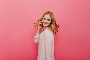 Confident girl in cotton pyjamas playing with her hair. Indoor photo of cheerful female model wears light-pink night-suit.