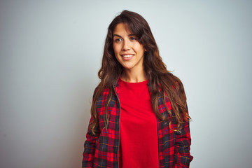 Young beautiful woman wearing red t-shirt and jacket standing over white isolated background looking away to side with smile on face, natural expression. Laughing confident.