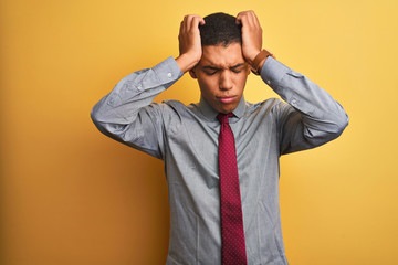 Young handsome arab businessman wearing shirt and tie over isolated yellow background suffering from headache desperate and stressed because pain and migraine. Hands on head.