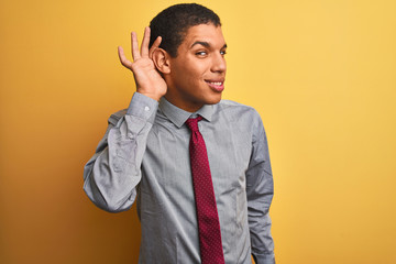 Young handsome arab businessman wearing shirt and tie over isolated yellow background smiling with hand over ear listening an hearing to rumor or gossip. Deafness concept.