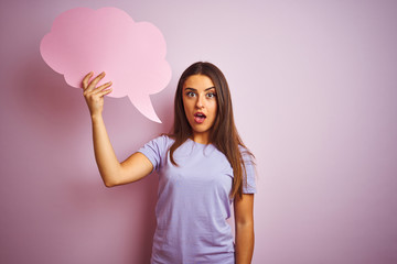 Young beautiful woman holding cloud speech bubble over isolated pink background scared in shock with a surprise face, afraid and excited with fear expression