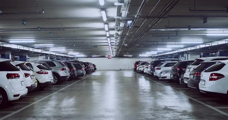 Zooming in view of big undeground parking garage at night. Drive through building parking lot with plenty of cars.
