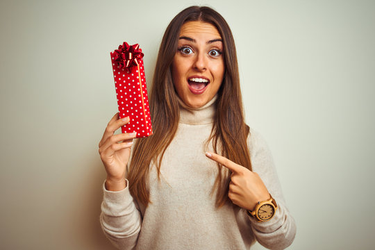 Young beautiful woman holding valentine gift standing over isolated white background very happy pointing with hand and finger