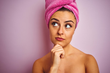 Young beautiful woman wearing towel after shower over isolated pink background serious face...