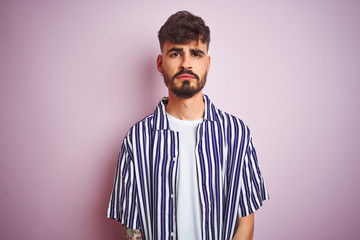 Young man with tattoo wearing striped shirt standing over isolated pink background depressed and worry for distress, crying angry and afraid. Sad expression.
