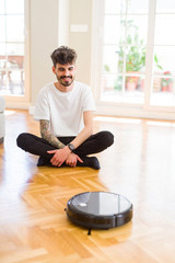 Young man using automatic vacuum cleaner to clean the floor, controling machine housework robot