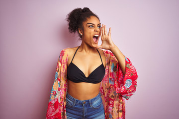 American woman on holiday wearing bikini and colorful dress over isolated pink background shouting and screaming loud to side with hand on mouth. Communication concept.