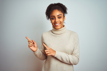 African american woman wearing winter turtleneck sweater over isolated white background smiling and looking at the camera pointing with two hands and fingers to the side.