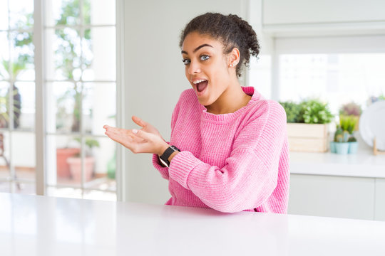 Beautiful african american woman with afro hair wearing casual pink sweater pointing aside with hands open palms showing copy space, presenting advertisement smiling excited happy