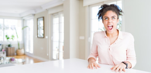 Wide angle of beautiful african american woman with afro hair angry and mad screaming frustrated and furious, shouting with anger. Rage and aggressive concept.