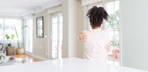 Wide angle of beautiful african american woman with afro hair Hugging oneself happy and positive from backwards. Self love and self care