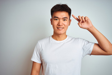 Young asian chinese man wearing t-shirt standing over isolated white background Smiling pointing to head with one finger, great idea or thought, good memory