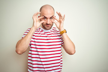 Young bald man with beard wearing casual striped red t-shirt over white isolated background Trying to open eyes with fingers, sleepy and tired for morning fatigue