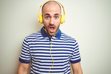 Young man listening to music wearing yellow headphones over isolated background afraid and shocked with surprise expression, fear and excited face.