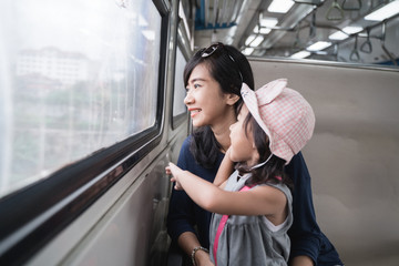Fototapeta premium mother and her daughter ride a train together and looking out the window