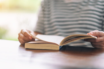 Closeup image of a woman holding and reading a vintage novel book on wooden table