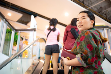 Fototapeta na wymiar Asian woman holding her purse standing on escalator which moving up in shopping mall