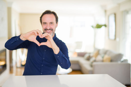 Handsome middle age man at home smiling in love showing heart symbol and shape with hands. Romantic concept.