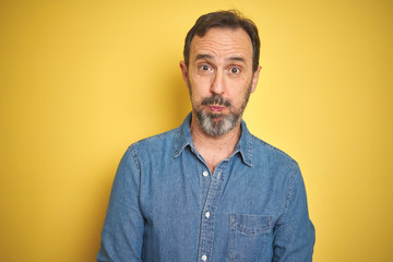 Fototapeta premium Handsome middle age senior man with grey hair over isolated yellow background puffing cheeks with funny face. Mouth inflated with air, crazy expression.