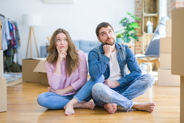Fototapeta na wymiar Young beautiful couple moving to a new house sitting on the floor with hand on chin thinking about question, pensive expression. Smiling with thoughtful face. Doubt concept.