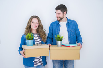 Young beautiful couple holding cardboard boxes very happy for moving to a new home over white isolated background
