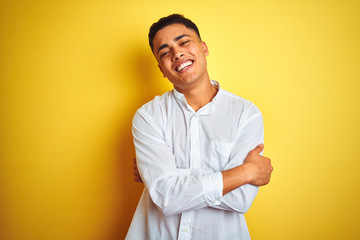 Young brazilian businessman wearing elegant shirt standing over isolated yellow background happy face smiling with crossed arms looking at the camera. Positive person.