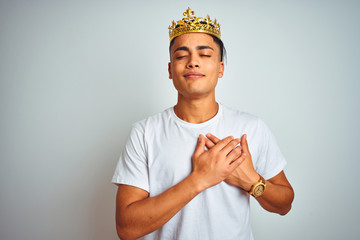 Young brazilian man wearing king crown standing over isolated white background smiling with hands...