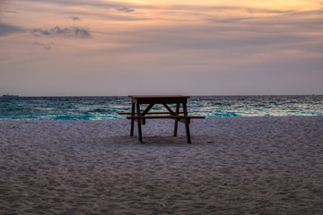 Fototapeta na wymiar This unique photo shows a table with a bench on a beach of the Maldives during a romantic sunset