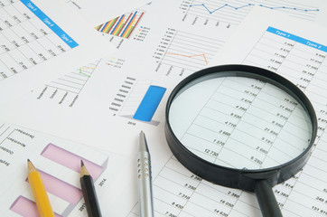 Business concept, magnifying glass pencils and pen on financial charts and graphs