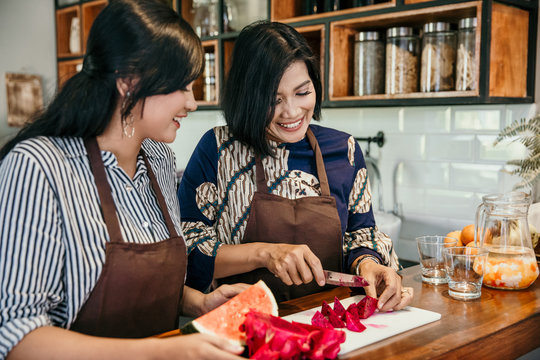 Two Asian Women Prepare To Cook And Slice Fruits In The Kitchen