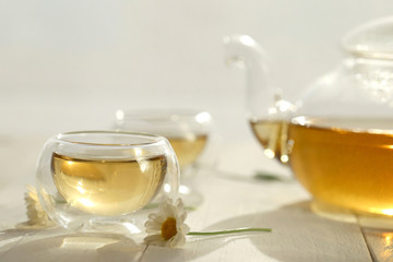 Chamomile tea.Organic natural chamomile tea in a  glass teapot and cups, chamomile flowers on a white wooden table.Herbal Green Teas