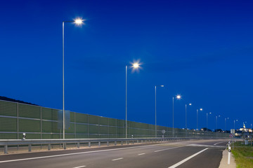 evening empty road with modern LED street light and noise barrier