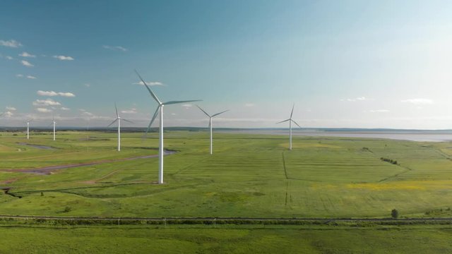 AERIAL: Flying paralell to group of powerful wind turbines on warm sunny day